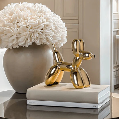 Gold balloon dog sculpture on books with a vase of white flowers in the background